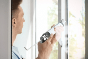 Man holding sealing gun and making window repairs