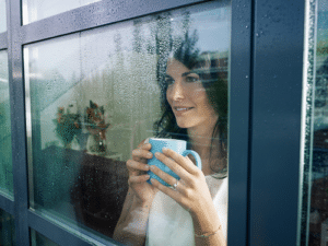 Woman holding teacup looking through home glass window