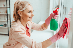 Woman wearing pink gloves and holding spray bottle while cleaning glass window