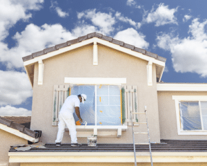 Painter standing on house roof in front of window
