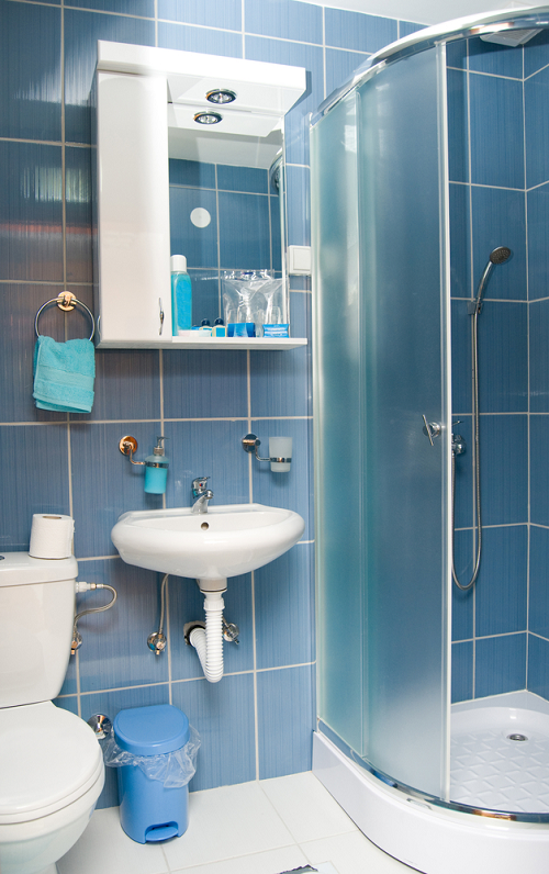 Bathroom with Blue tiles, Frosted glass enclosed shower, white toilet, sink and cabinet